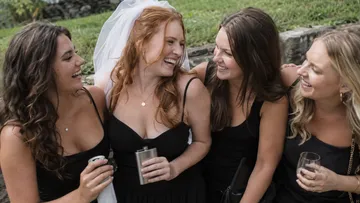 Four women smiling, holding drinks outdoors.