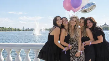 Five women hugging by a lake, holding balloons.
