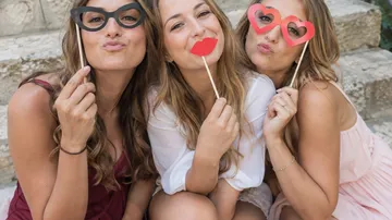 Three women holding playful photo props outdoors.