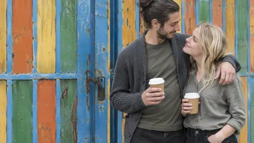 Couple holding coffee cups, smiling outside.