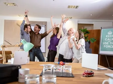 Five people celebrate happily in a modern office space.