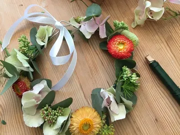 Blumenkranz liegt auf Holztisch, umgeben von Werkzeugen.