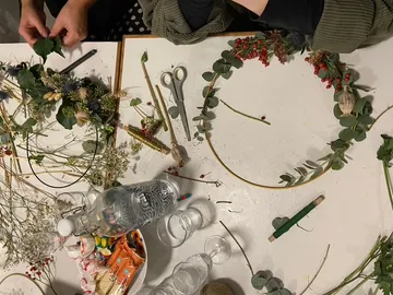 Blumenkranz wird mit Pflanzenmaterialien auf einem Tisch gestaltet.
