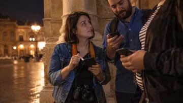 Three people using phones outside at night.