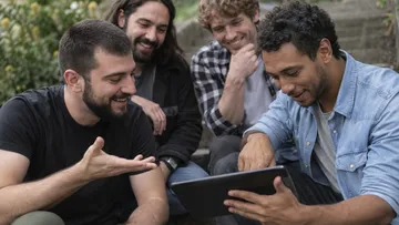 Gruppe von Männern lächelt auf Tablet im Freien.