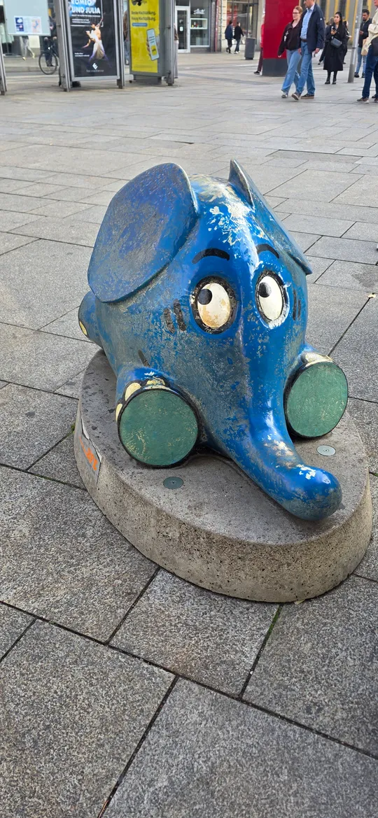Blaue Elefantenskulptur auf Steinplattform draußen.