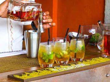 Bartender pours rum into glasses with cocktails.