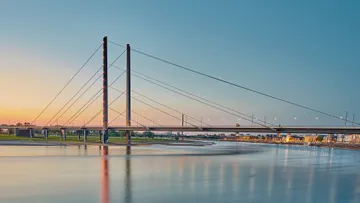 Schrägseilbrücke überspannt ruhigen Fluss bei Sonnenuntergang.