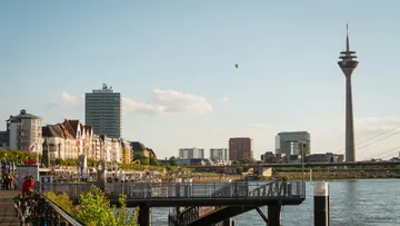 Riverfront promenade with tower and cityscape.