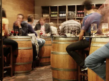 Holzfässer, Menschen essen und trinken in einer Bar.