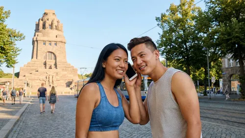 Zwei Personen teilen ein Handy, Denkmal im Hintergrund.