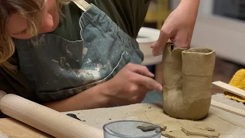 Person shaping clay pot on table.
