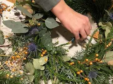 Eine Hand gestaltet einen Kranz aus verschiedenen Pflanzen.