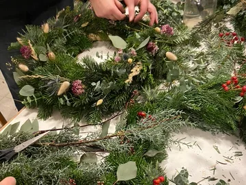 Kranz wird mit grünen Zweigen und Blumen gestaltet.