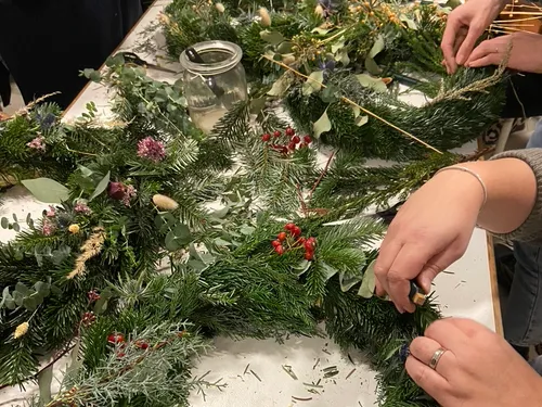 People crafting wreaths with greenery on table.