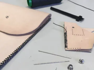 Light-colored leather products lie on a table, partially finished.