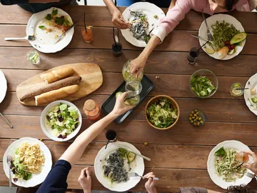 Gemeinsame Mahlzeit am Tisch mit Salaten und Getränken.