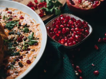 Hummus mit Granatapfelkernen, auf grünem Tuch serviert.