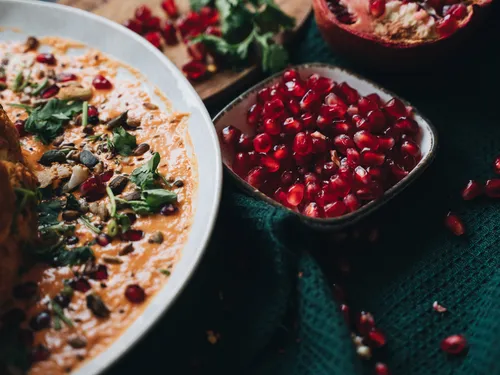 Hummus with pomegranate seeds, served on a green towel.