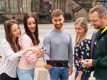 Fünf Personen schauen auf ein Tablet im Freien.