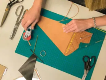 One hand is cutting leather on a green cutting board.
