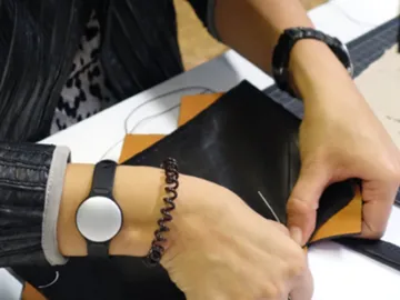 Hands sew orange parts onto black material.