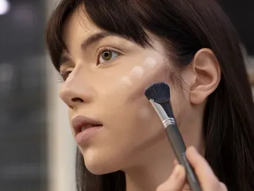 A woman receives makeup on her face in a modern space.