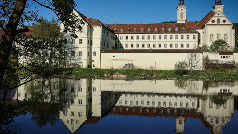 A building is reflected in the calm water of a river.