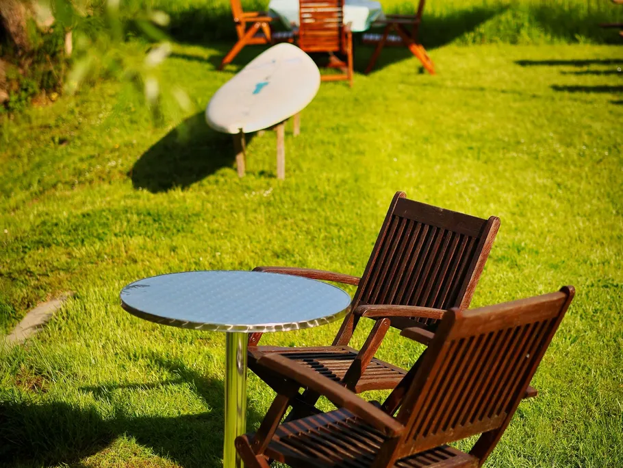 Wooden table and chairs are placed on green lawn in the sun.