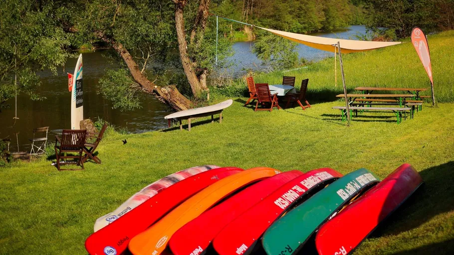 Colourful canoes lie on the grass at the riverbank.