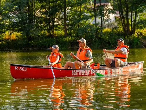 Three people in a canoe are paddling on a calm body of water.