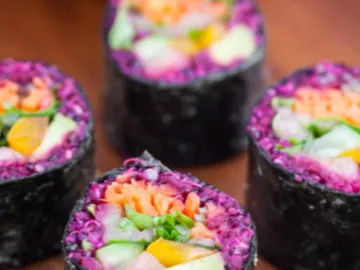 Bunte Sushi-Rollen liegen auf einem Holzbrett.