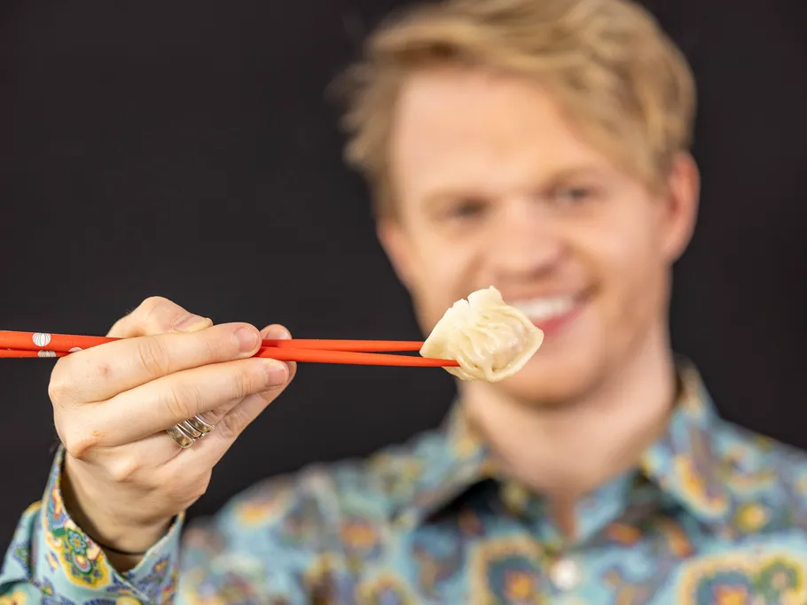 A man holds a steam noodle in front of him with chopsticks.