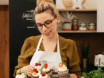 Frau hält dekorierte Cupcakes in einer Küchenumgebung.