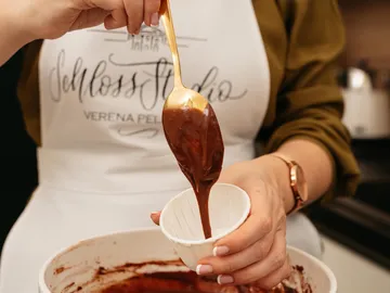 A spoon with chocolate dough fills a cup in the kitchen environment.