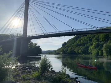 Kanute paddelt ruhig unter einer Hängebrücke im Fluss.