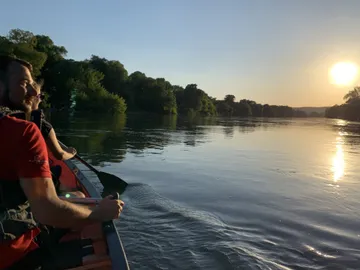 Kanu fährt ruhig auf einem spiegelnden Fluss bei Sonnenuntergang.