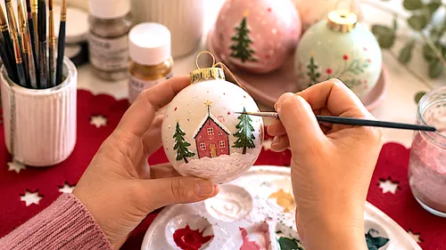 Hands painting Christmas ornament in festive setting.