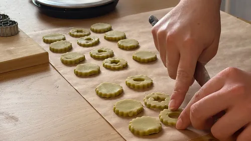 Hands shaping cookies on parchment paper.