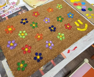 Decorated doormat with colorful flowers, painting supplies.