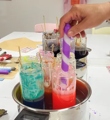 Hand taucht Kerze in bunte Wachsgläser.
