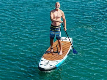 Man stands on a paddleboard in water and paddles.