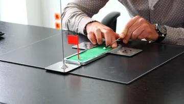 Person playing miniature golf on desk.