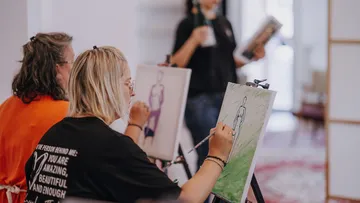 Two women painting on canvases indoors.