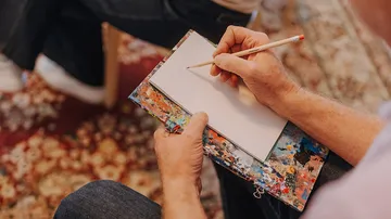 Person drawing on paper, sitting on carpet.