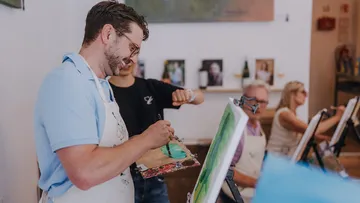 Man painting, smiling, in an art class.