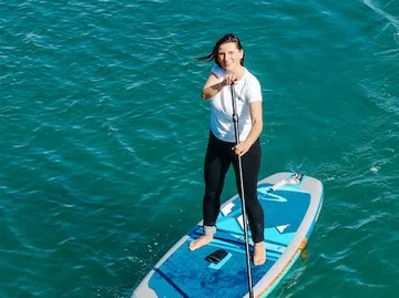 Woman stands on a paddleboard and paddles in the water.