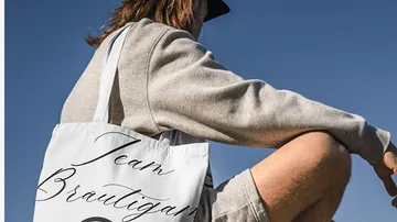 Person sitzt mit Tragetasche draußen.