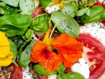 Colourful flowers and basil decorate fresh tomato slices.