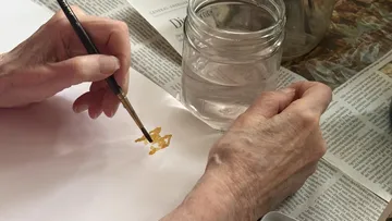 Hands painting on paper with water jar nearby.